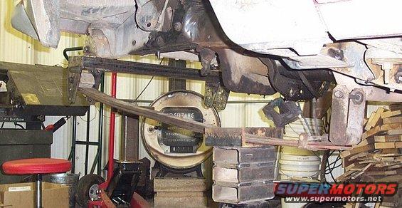Leaf spring suspension assembly on a vehicle, possibly from the 1980s, with a scale in the background