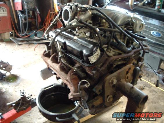 Engine on a stand with an oil drain pan underneath. Some tools and equipment are in the background