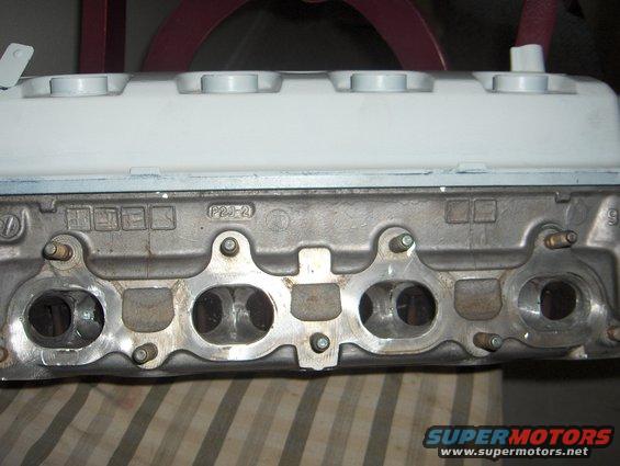 Close-up of an engine cylinder head with intake and exhaust ports visible. Some text is cast into the metal