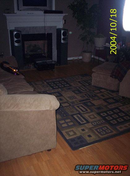 Living room with fireplace, speakers, couch, rug, and potted plant. Date stamp 2004/10/18
