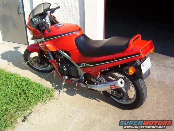 Red Kawasaki EX motorcycle with black seat and silver exhaust pipe, parked on concrete