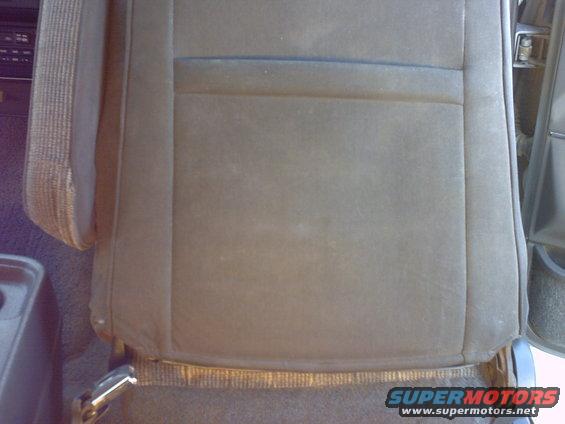 Car seat with worn fabric and visible stitching. A portion of the dashboard is visible on the left