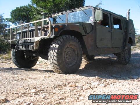 Olive drab Humvee with brush guard and large tires parked on a dirt road