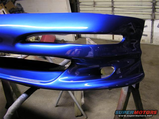 Blue car bumper with large air intakes, resting on sawhorses