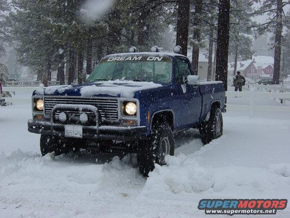 Blue 1979 Chevrolet C/K Pickup driving through snow with 'DREAM ON' banner on windshield