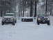 1979 Chevrolet C/K Pickup - Two pickup trucks are parked in a snowy landscape with trees and houses in the background.