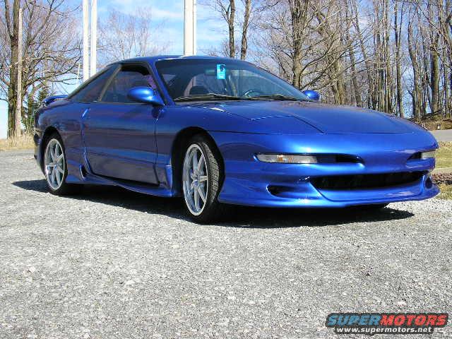 Blue 1994 Ford Probe GT coupe, front 3/4 view, custom body kit, aftermarket wheels, parked on gravel