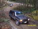 1987 Jeep Cherokee - A dark blue 1987 Jeep Cherokee navigates a muddy off-road trail with another vehicle visible in the background.