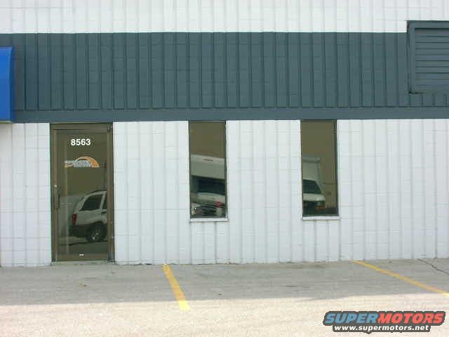 White SUV parked inside a building, seen through a glass door