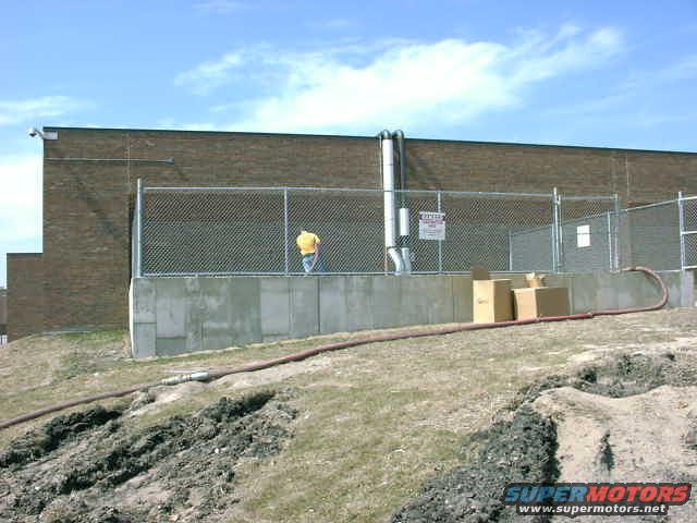 Blower pipes and a man in a yellow shirt near a chain-link fence