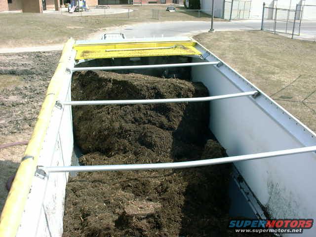 Dump truck bed filled with mulch, yellow tarp visible