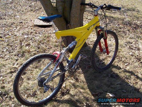 Yellow full-suspension mountain bike leaning against a tree, rear three-quarter view