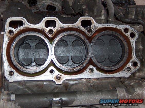 Close-up of engine cylinder head showing three pistons inside cylinders