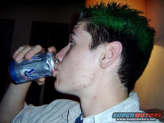 Person with green spiked hair drinks from a crushed can. Watermark reads SUPERMOTORS.NET