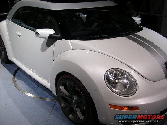 White Volkswagen Beetle convertible with silver racing stripes and red trim on wheels, viewed from the front right