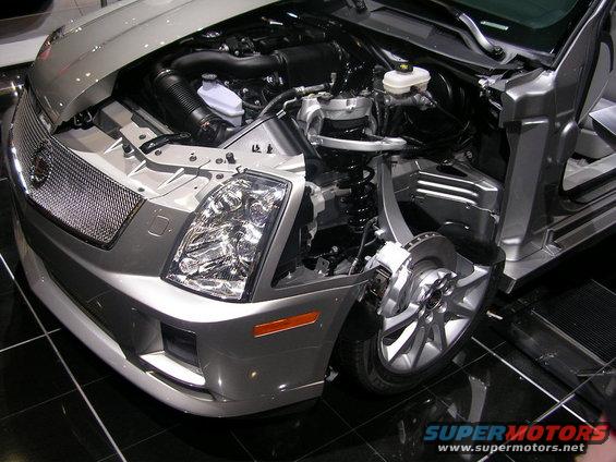 Silver car front end with hood open, revealing engine and suspension components. Headlight and grille visible