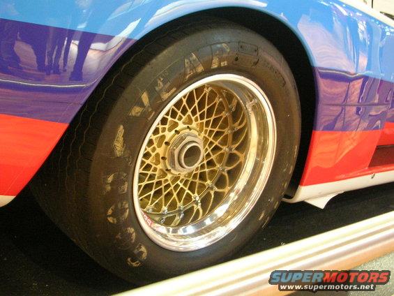 Gold mesh wheel and tire on a car with red, blue, and white racing stripes