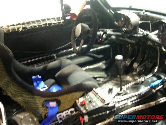 Racing bucket seat with blue harness, steering wheel, and shifter in a modified car interior