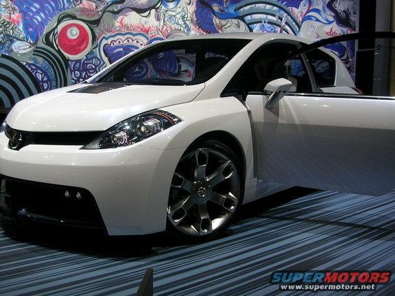 White concept car with open driver's door, custom wheels, and abstract mural in background