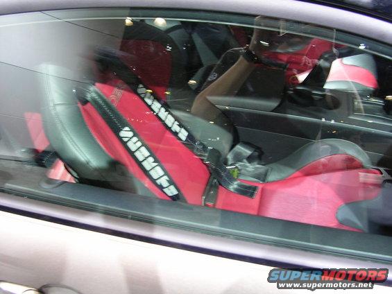 Close-up of a red racing seat with black harness straps that have white lettering