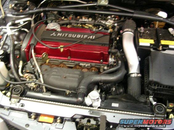 Engine bay with red Mitsubishi engine cover, silver intake pipe, and battery