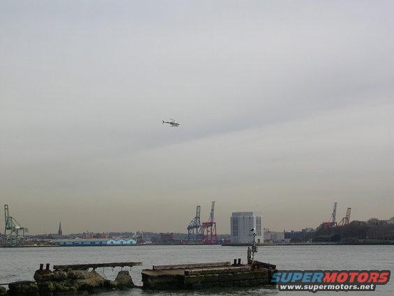 Helicopter flying over a harbor with cranes and buildings in the background