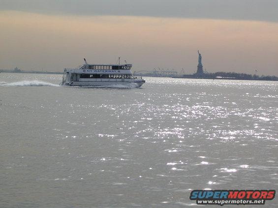 Ferry boat labeled NY WATERWAY moving on water, Statue of Liberty visible in distance