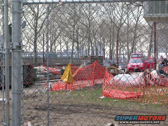 Construction site with orange netting and a red car parked behind a chain-link fence