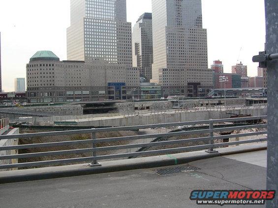 Construction site with large buildings in the background and a metal railing in the foreground