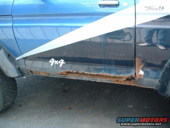 Blue SUV door with extensive rust on the lower panel and a white stripe graphic. '4x4' decal visible