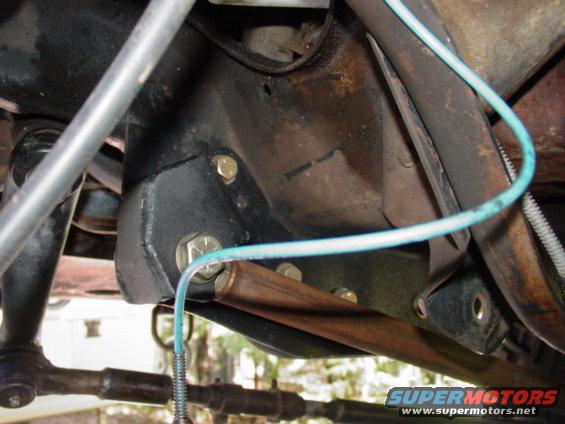 Close-up of a black metal bracket with bolts and a blue wire attached, part of a vehicle's suspension system