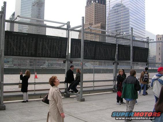 Memorial display boards with names, people, and tall buildings