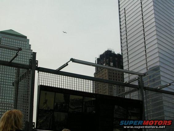 New York City skyline with skyscrapers, an airplane in the sky, and a fence in the foreground