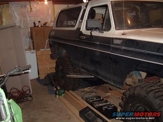 Modified Ford Bronco with large tires and side pipes, parked indoors