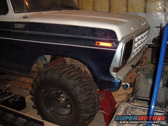 Front quarter of a 1979 Ford Bronco with large off-road tires, parked indoors