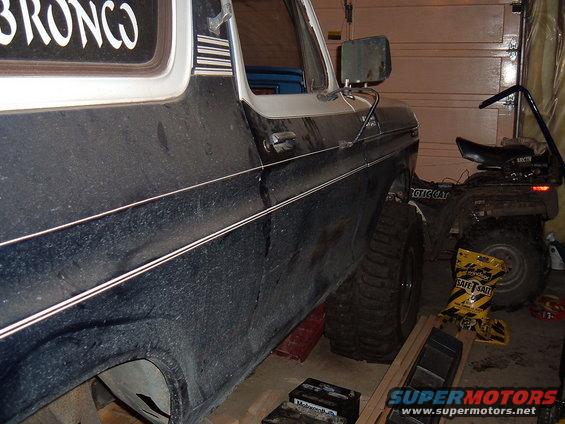 Side view of a dark blue 1979 Ford Bronco with large tires. An ATV is parked behind it