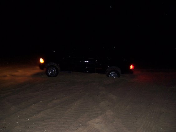 Black pickup truck stuck in sand at night, side view