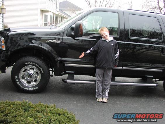 Black 2005 Ford Excursion SUV, side view, with a young boy pointing at the door