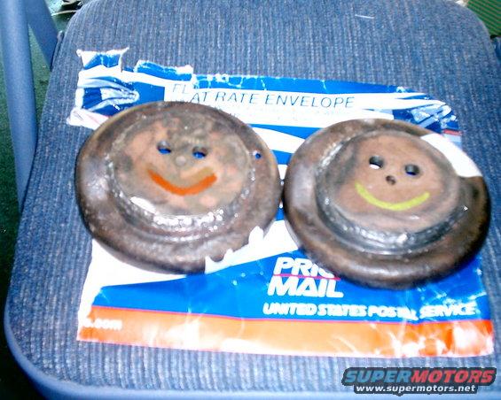 Two rusty brake rotors with drawn-on smiley faces sit on a blue USPS flat rate envelope