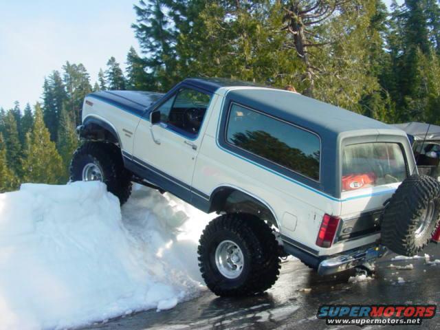 White and blue 1986 Ford Bronco climbing snow bank
