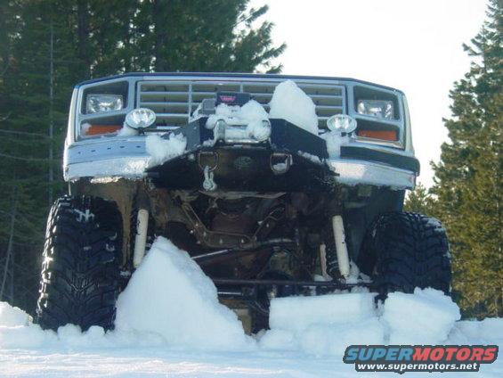 Front view of a lifted Ford Bronco with a winch and plow attachment stuck in snow