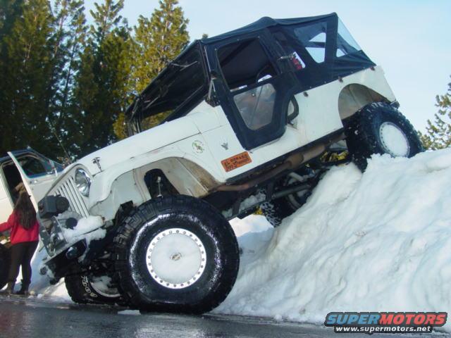 White Jeep Wrangler climbing a snow bank, driver's door open