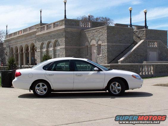 White sedan parked on concrete, side view. Building with stone facade and arched windows in background