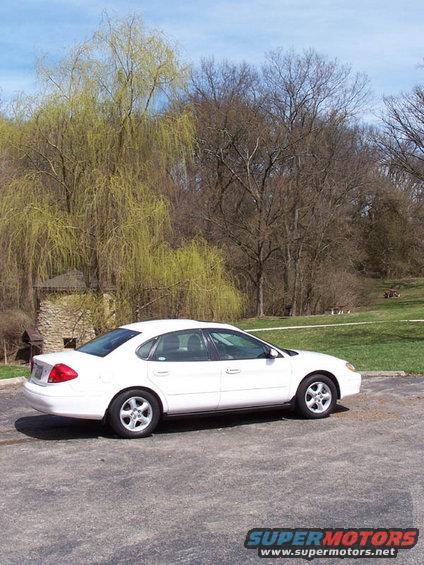 White sedan parked on asphalt with trees and grass in background