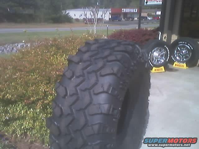 Off-road tire in foreground, two chrome wheels with yellow stands behind