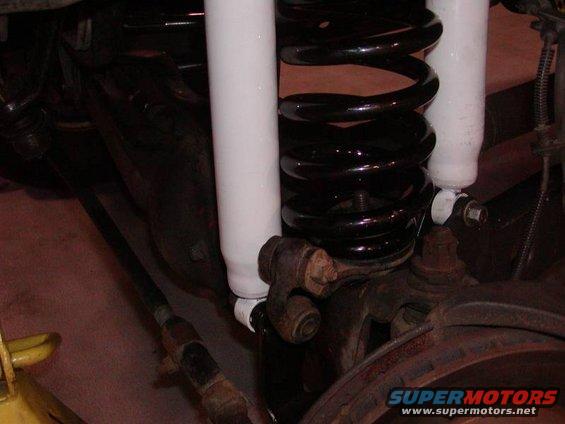 Close-up of black coil spring and white shock absorber assembly with suspension linkage