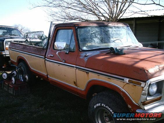 Rusty two-tone pickup truck parked next to another truck. Some items in the truck bed