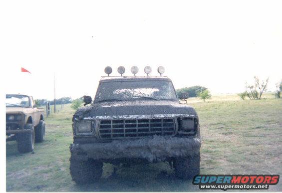 Mud-covered 1979 Ford Bronco front view with light bar and another vehicle to the left