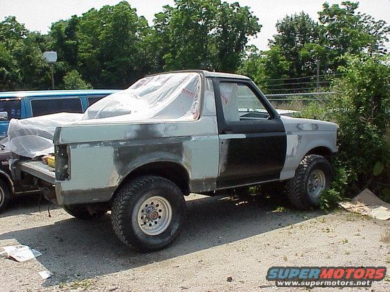 Ford Bronco in primer, covered with plastic sheeting in the rear. Bodywork is in progress