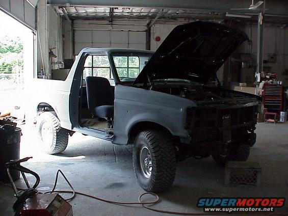 Ford Bronco with hood open, doors open, in a garage, appears to be undergoing repairs or restoration